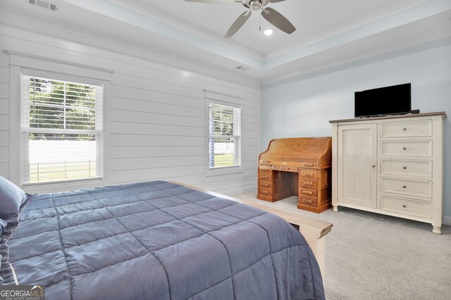 bedroom featuring multiple windows, light carpet, a tray ceiling, and ceiling fan