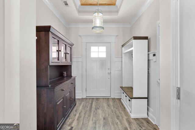 mudroom with light wood-type flooring, a raised ceiling, and crown molding