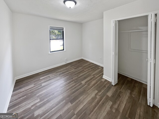 unfurnished bedroom with a closet, a textured ceiling, and dark wood-type flooring