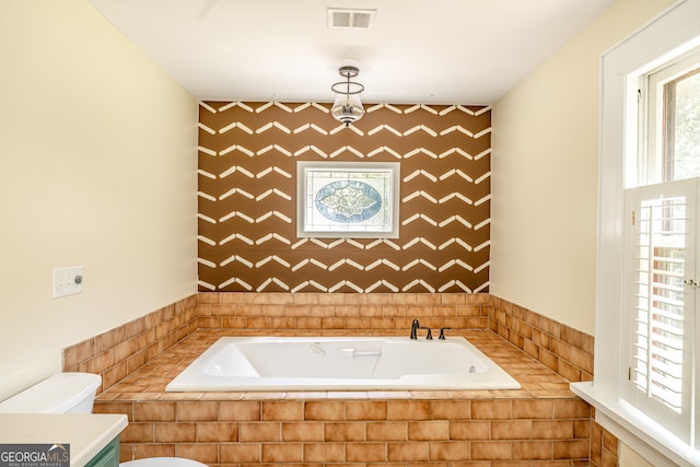 bathroom featuring a relaxing tiled tub, toilet, and vanity