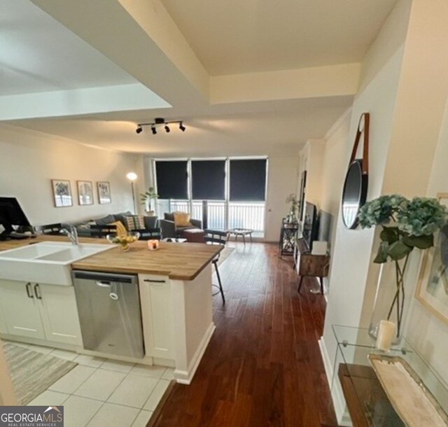 kitchen with light tile patterned floors, butcher block counters, track lighting, dishwasher, and white cabinetry