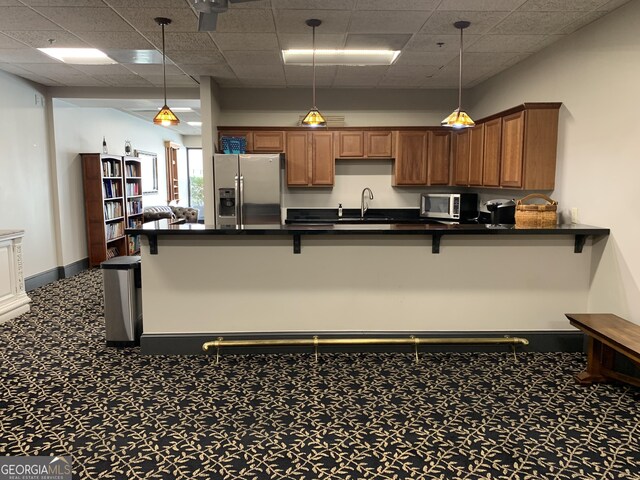 kitchen featuring a drop ceiling, stainless steel appliances, hanging light fixtures, and carpet flooring