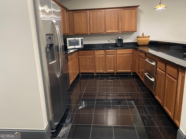 kitchen with stainless steel fridge, dark countertops, white microwave, brown cabinets, and hanging light fixtures