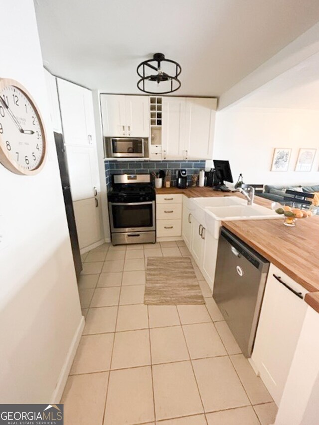 kitchen featuring decorative backsplash, white cabinetry, butcher block counters, light tile patterned floors, and stainless steel appliances