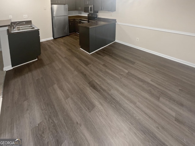 kitchen featuring a peninsula, dark wood-type flooring, a sink, appliances with stainless steel finishes, and dark countertops