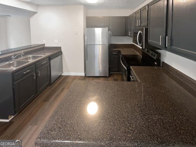 kitchen featuring appliances with stainless steel finishes, dark wood-style flooring, a sink, and a peninsula