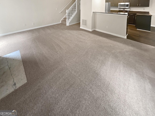 unfurnished living room with stairway, baseboards, visible vents, and dark carpet