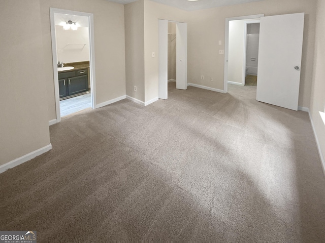 unfurnished bedroom featuring baseboards, ensuite bathroom, a sink, carpet floors, and a closet