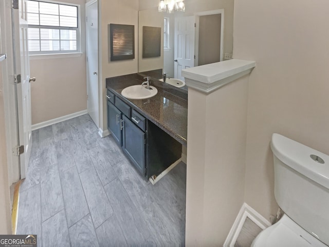 bathroom featuring a notable chandelier, toilet, vanity, wood finished floors, and baseboards