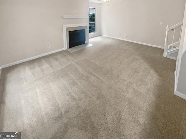 unfurnished living room featuring carpet, stairs, baseboards, and a fireplace with flush hearth