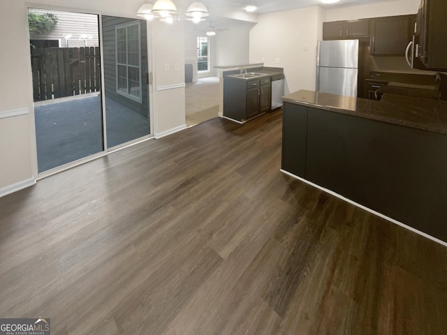 kitchen with dark wood finished floors, dark countertops, open floor plan, stainless steel appliances, and a sink