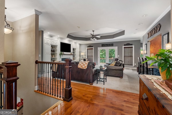 living room featuring light hardwood / wood-style floors, crown molding, ceiling fan, and a tray ceiling