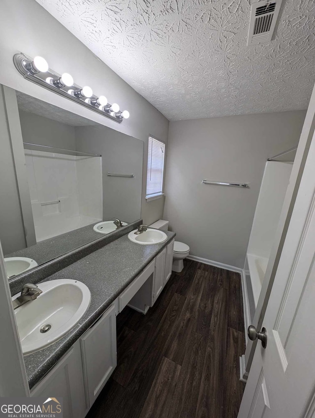 full bathroom featuring a textured ceiling, double sink vanity, wood-type flooring, toilet, and washtub / shower combination