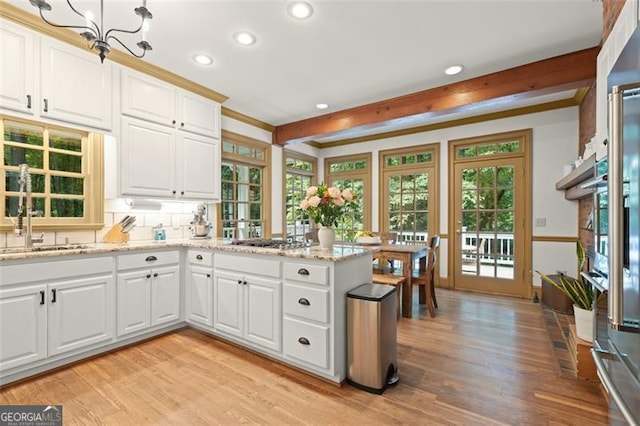 kitchen with a notable chandelier, light hardwood / wood-style flooring, light stone counters, kitchen peninsula, and white cabinets