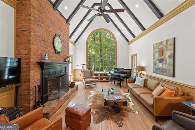 living room featuring beamed ceiling, high vaulted ceiling, a brick fireplace, ceiling fan, and light wood-type flooring