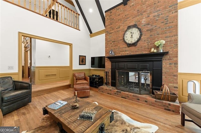 living room featuring beamed ceiling, high vaulted ceiling, a brick fireplace, and light hardwood / wood-style floors