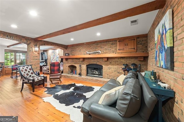 living room with light wood-type flooring, a fireplace, beamed ceiling, and brick wall