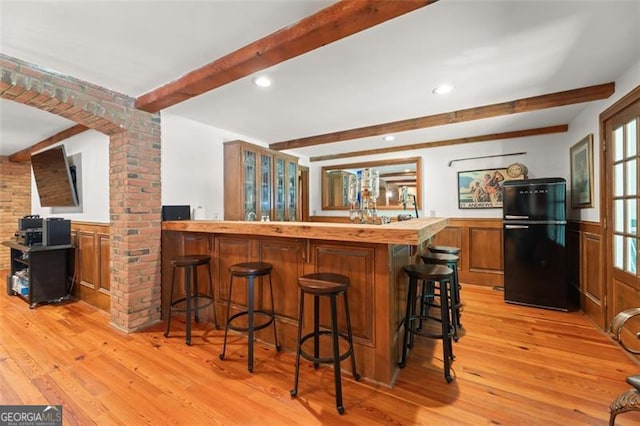 kitchen with a kitchen bar, light hardwood / wood-style flooring, kitchen peninsula, and black fridge