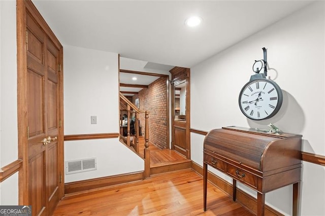 corridor with brick wall and light hardwood / wood-style flooring