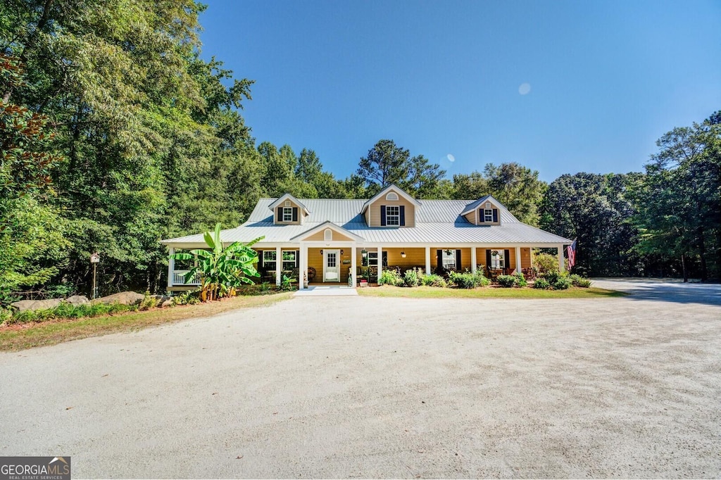 view of front facade featuring covered porch, metal roof, and dirt driveway