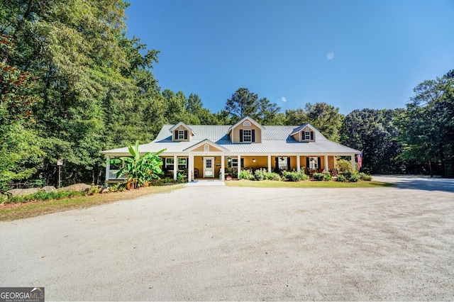 view of front facade featuring covered porch, metal roof, and dirt driveway