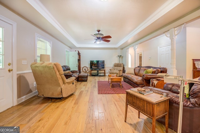 living room with ceiling fan, a raised ceiling, ornamental molding, and light wood-type flooring