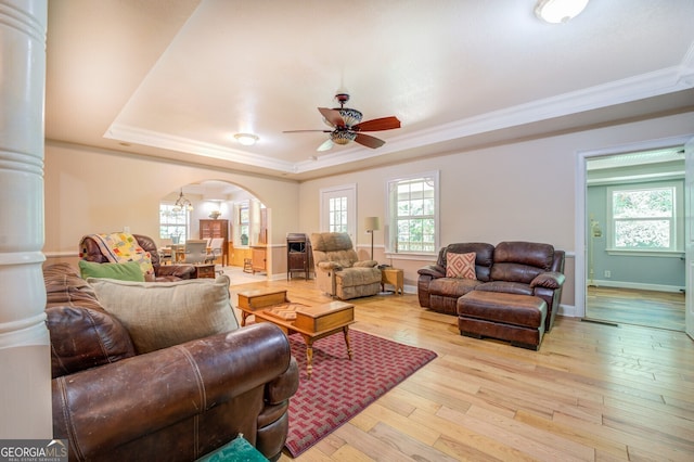 living room with light wood-type flooring, ornamental molding, ceiling fan, and a tray ceiling