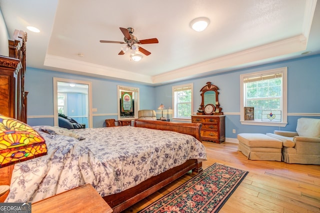 bedroom with ceiling fan, a raised ceiling, light hardwood / wood-style floors, and crown molding