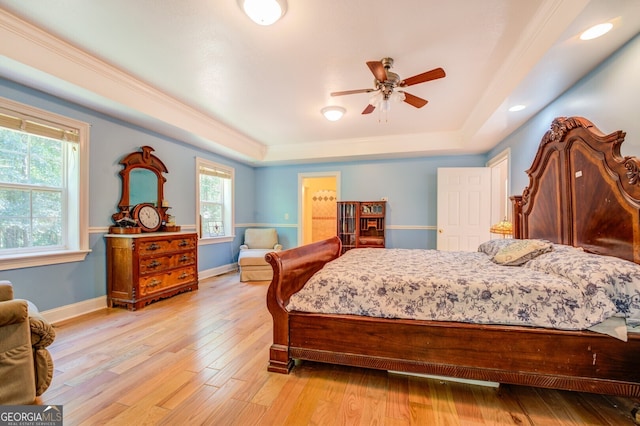 bedroom with ceiling fan, a raised ceiling, light hardwood / wood-style flooring, and multiple windows