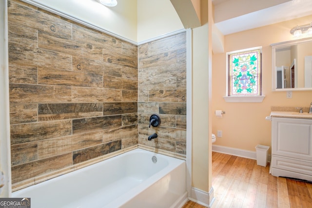 full bathroom with hardwood / wood-style flooring, tiled shower / bath, vanity, and toilet