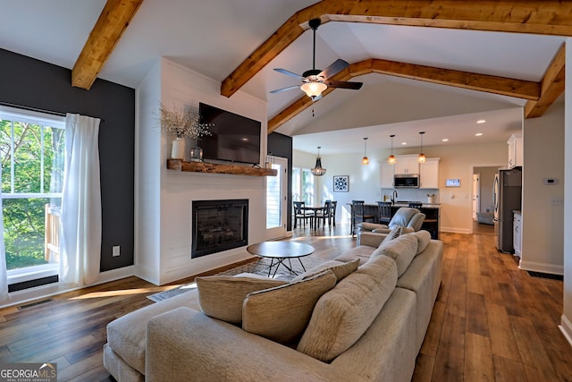 living room featuring a healthy amount of sunlight, dark wood-type flooring, a large fireplace, and beam ceiling