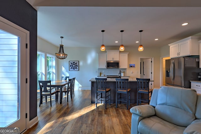 kitchen with appliances with stainless steel finishes, light stone counters, white cabinets, hanging light fixtures, and a breakfast bar area