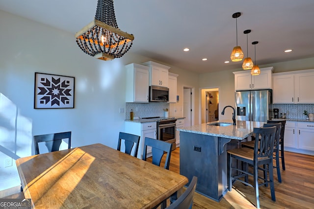 kitchen featuring sink, white cabinetry, stainless steel appliances, and an island with sink