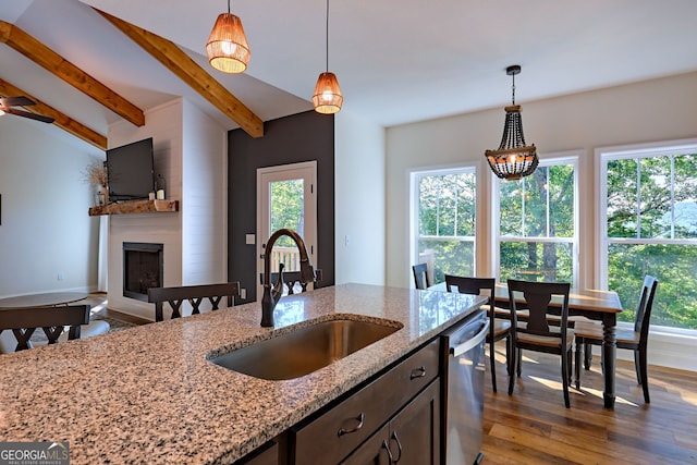 kitchen with hanging light fixtures, light stone countertops, sink, dishwasher, and dark wood-type flooring