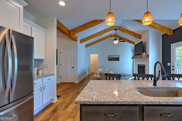 kitchen with sink, white cabinetry, stainless steel fridge, and light stone counters