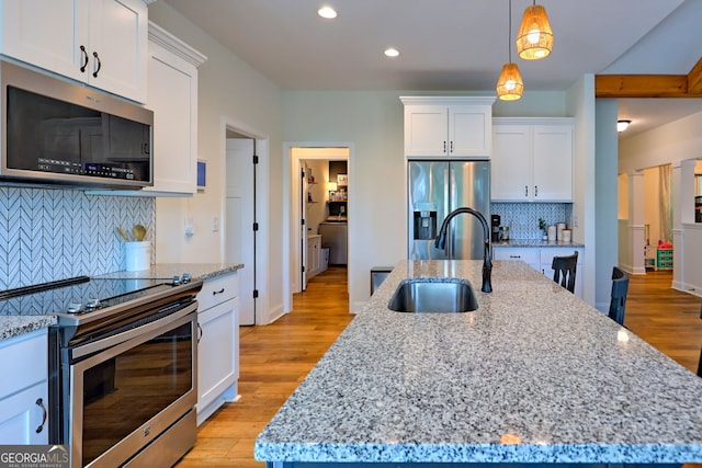 kitchen featuring sink, light stone counters, stainless steel appliances, white cabinets, and a kitchen island with sink