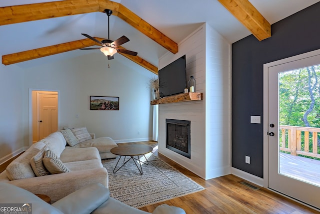 living room with ceiling fan, a large fireplace, lofted ceiling with beams, and light wood-type flooring