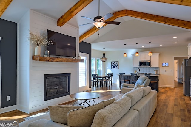 living room with vaulted ceiling with beams, sink, a large fireplace, dark hardwood / wood-style floors, and ceiling fan