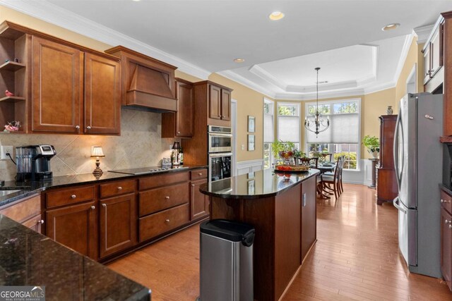 kitchen with stainless steel appliances, light hardwood / wood-style flooring, custom range hood, and a tray ceiling