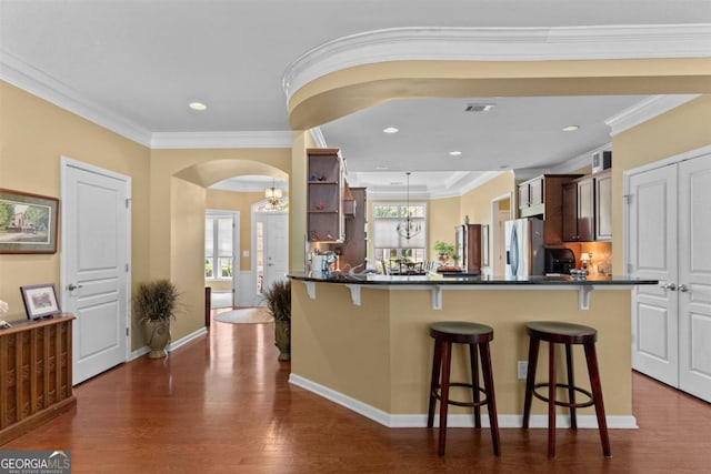 kitchen with a kitchen bar, stainless steel refrigerator with ice dispenser, crown molding, kitchen peninsula, and dark wood-type flooring