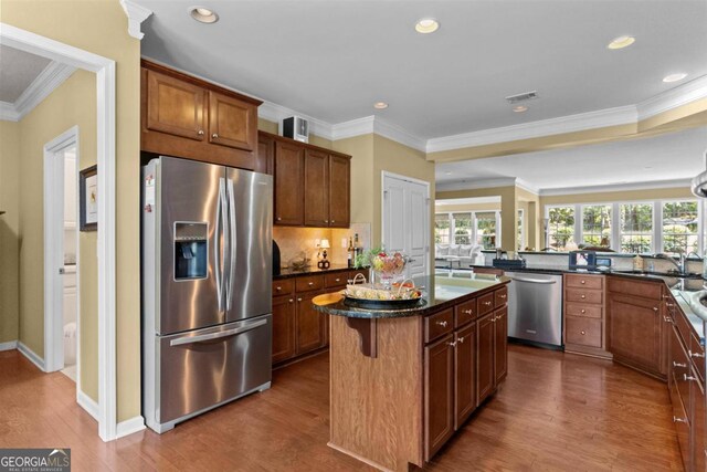 kitchen featuring dark stone counters, appliances with stainless steel finishes, dark hardwood / wood-style floors, a kitchen island, and crown molding