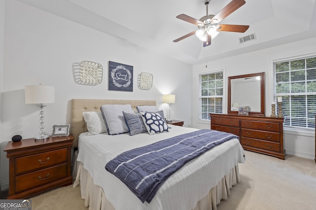 bedroom featuring ceiling fan, a raised ceiling, light carpet, and multiple windows