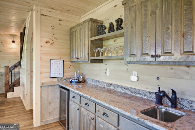 kitchen featuring sink, light hardwood / wood-style floors, wooden ceiling, wooden walls, and beverage cooler