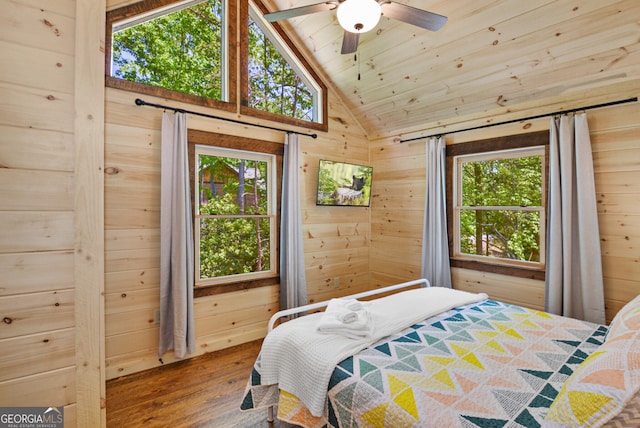 bedroom with wood walls, vaulted ceiling, hardwood / wood-style flooring, and ceiling fan