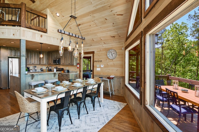 dining area featuring hardwood / wood-style floors, a wealth of natural light, high vaulted ceiling, and wooden walls