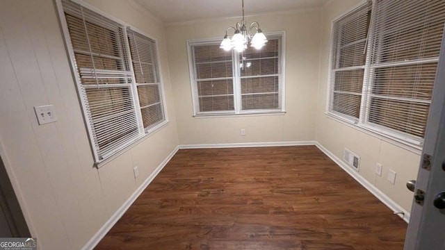 unfurnished dining area featuring dark hardwood / wood-style flooring, crown molding, and a chandelier