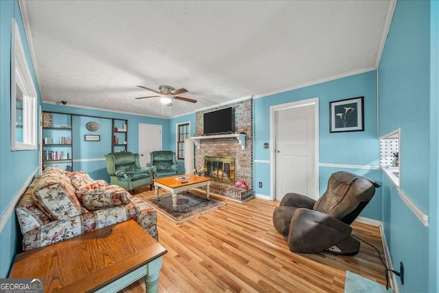 living room featuring a brick fireplace, light hardwood / wood-style floors, ceiling fan, crown molding, and brick wall