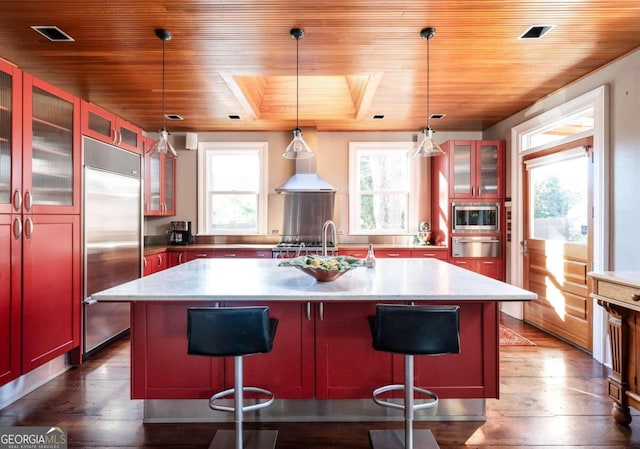 kitchen with hanging light fixtures, dark wood-type flooring, built in appliances, wooden ceiling, and a kitchen island with sink