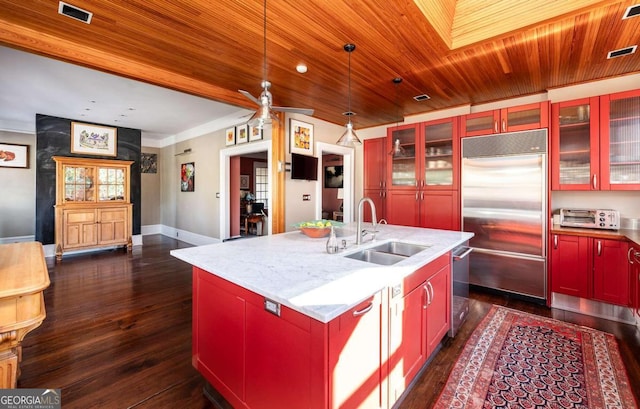 kitchen featuring light stone counters, dark hardwood / wood-style floors, sink, an island with sink, and appliances with stainless steel finishes