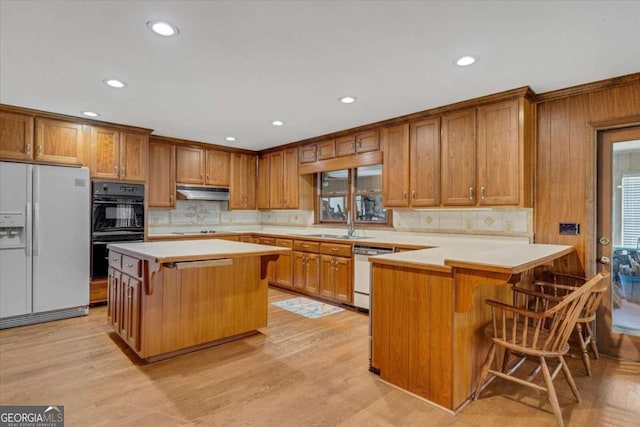 kitchen featuring light hardwood / wood-style floors, tasteful backsplash, black appliances, a kitchen island, and a breakfast bar area